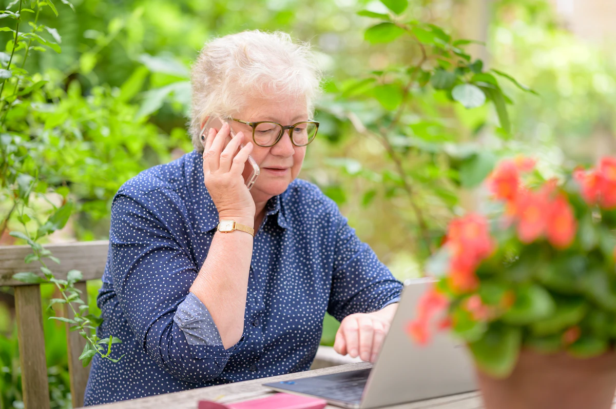 Oudere vrouw zit buiten met haar laptop en telefoon